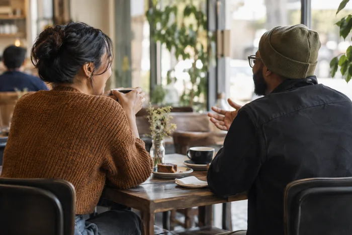 Two people chatting over coffee at a café table, shown from behind