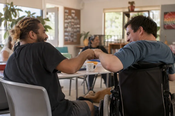 A small group at a table, one using a wheelchair, sharing a fist bump and a laugh together